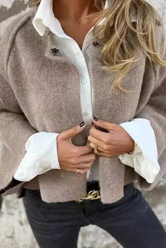 Donna con giacca beige in lana, camicia bianca e jeans neri. Moda autunnale elegante, stile casual chic, dettagli di anelli e cintura dorata.