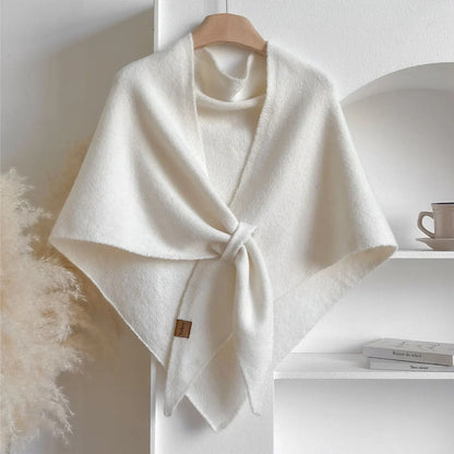 Scialle bianco in lana morbida appeso su gruccia, elegante e caldo, ideale per l'inverno. Sfondo minimalista con tazza e libri su mensola.