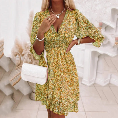 Donna con abito floreale giallo-verde, borsa bianca a tracolla, collana e bracciale, in ambiente elegante. Moda femminile, stile estivo.