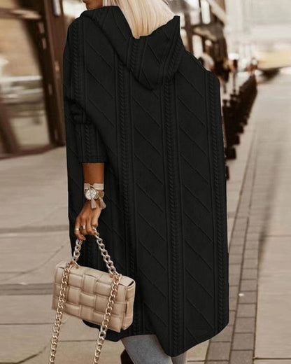 Donna con cappotto lungo nero a maglia, borsa beige a catena, cammina in città. Moda autunnale, stile urbano, abbigliamento casual elegante.