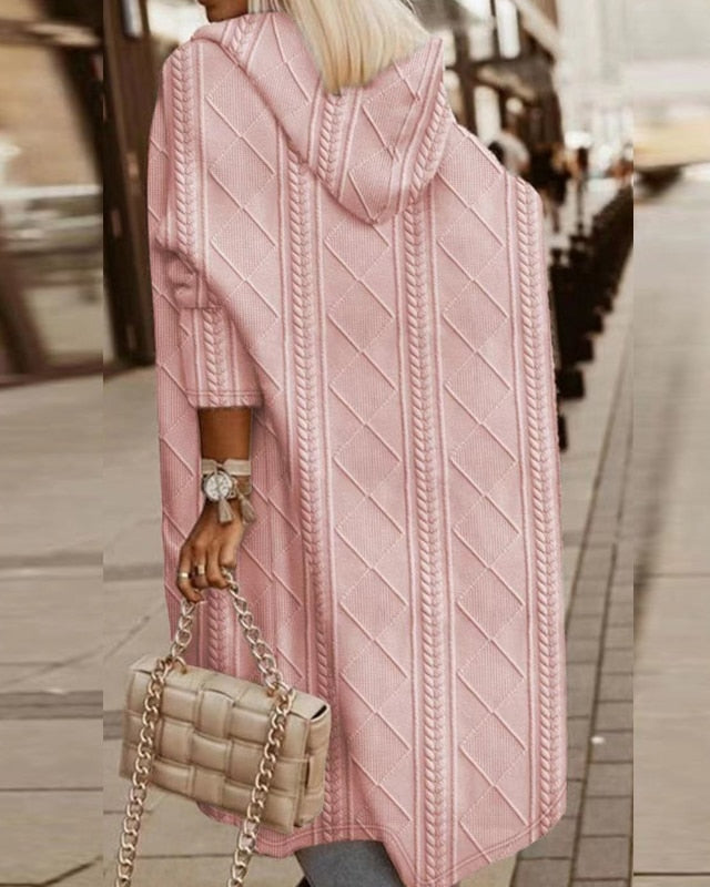 Donna con cappotto rosa a maglia con cappuccio, motivo a rombi, cammina in città. Borsa beige intrecciata a catena. Moda autunnale elegante.