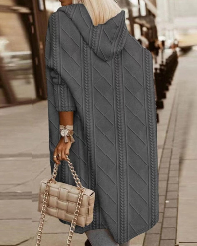 Donna con cappotto lungo grigio a maglia, borsa a catena beige, strada urbana. Moda autunnale, stile casual chic, tendenze abbigliamento femminile.