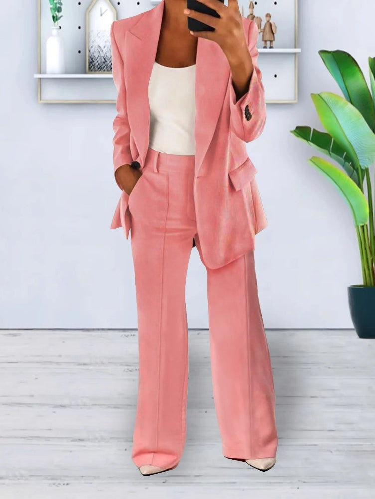 Donna in elegante completo rosa, giacca e pantaloni, con top bianco. Outfit moda femminile, stile business casual. Pianta verde sullo sfondo.