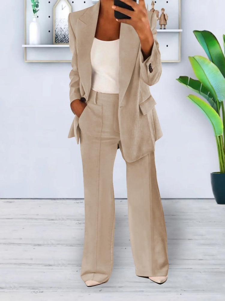 Donna in elegante completo beige, giacca e pantaloni, con top bianco. Sfondo moderno con piante e decorazioni. Moda femminile, abbigliamento formale.