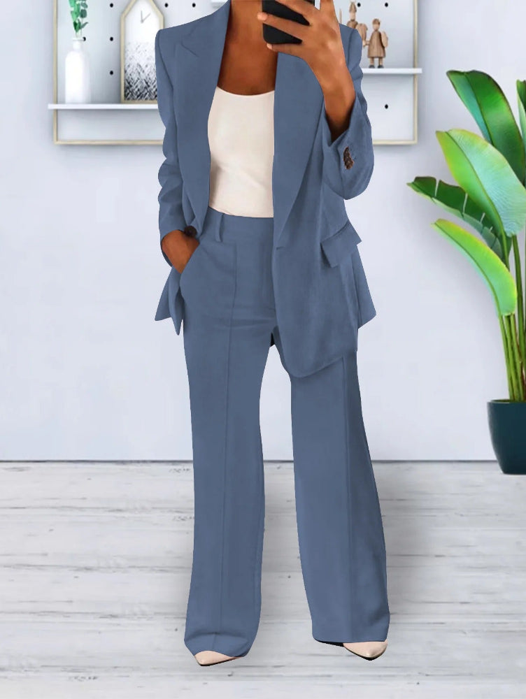 Donna in completo blu elegante, giacca e pantaloni, con top bianco. Sfondo moderno con pianta verde e decorazioni minimaliste. Moda business casual.