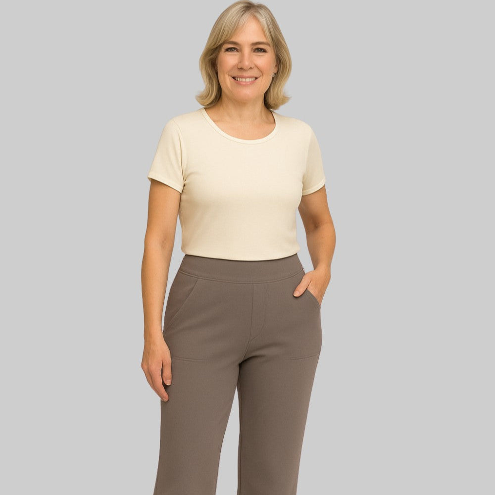 Donna sorridente con maglietta beige e pantaloni marroni su sfondo grigio. Moda casual, abbigliamento femminile, stile elegante.
