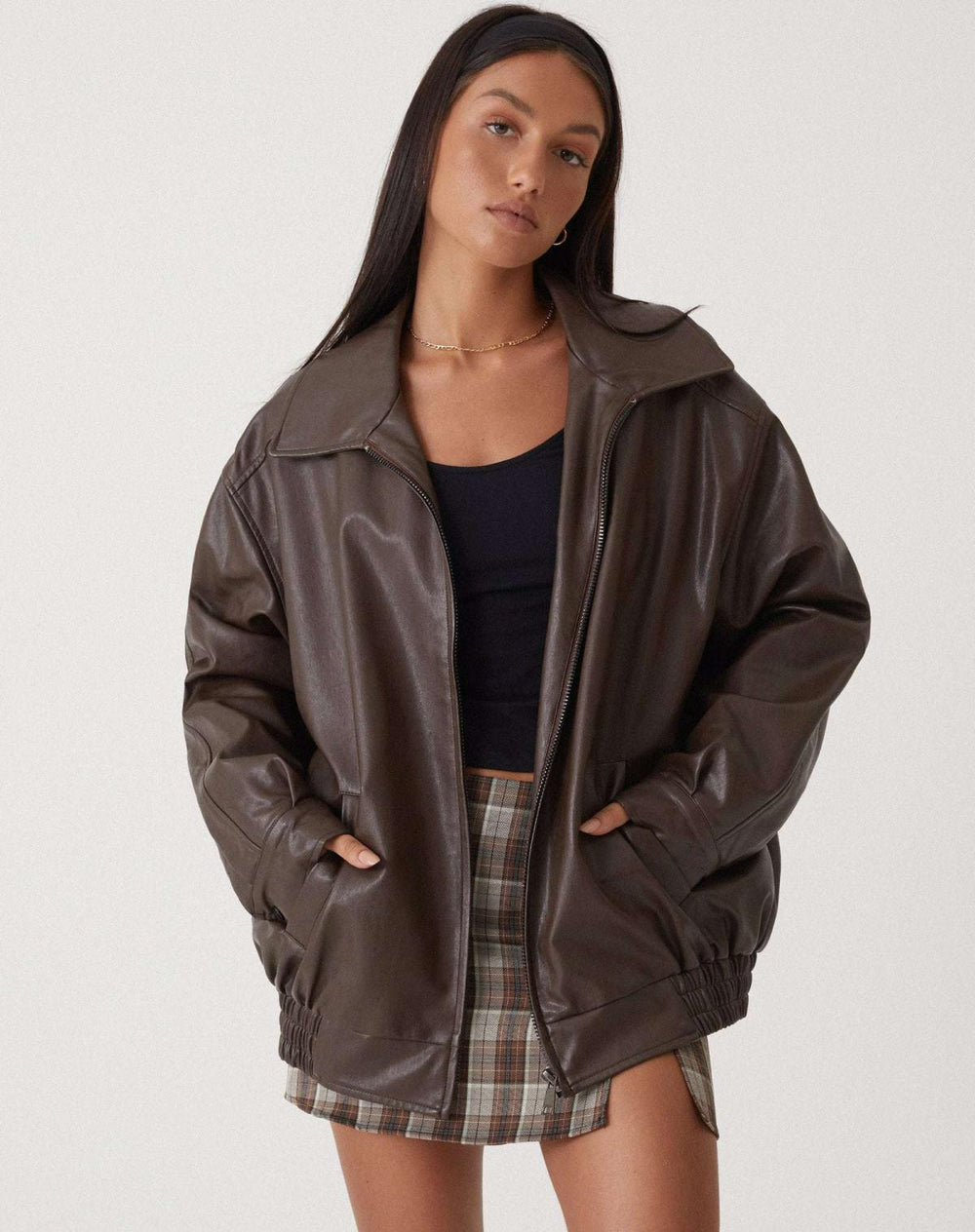Donna con giacca di pelle marrone oversize, top nero e gonna a quadri. Moda autunnale, stile casual chic, abbigliamento femminile trendy.